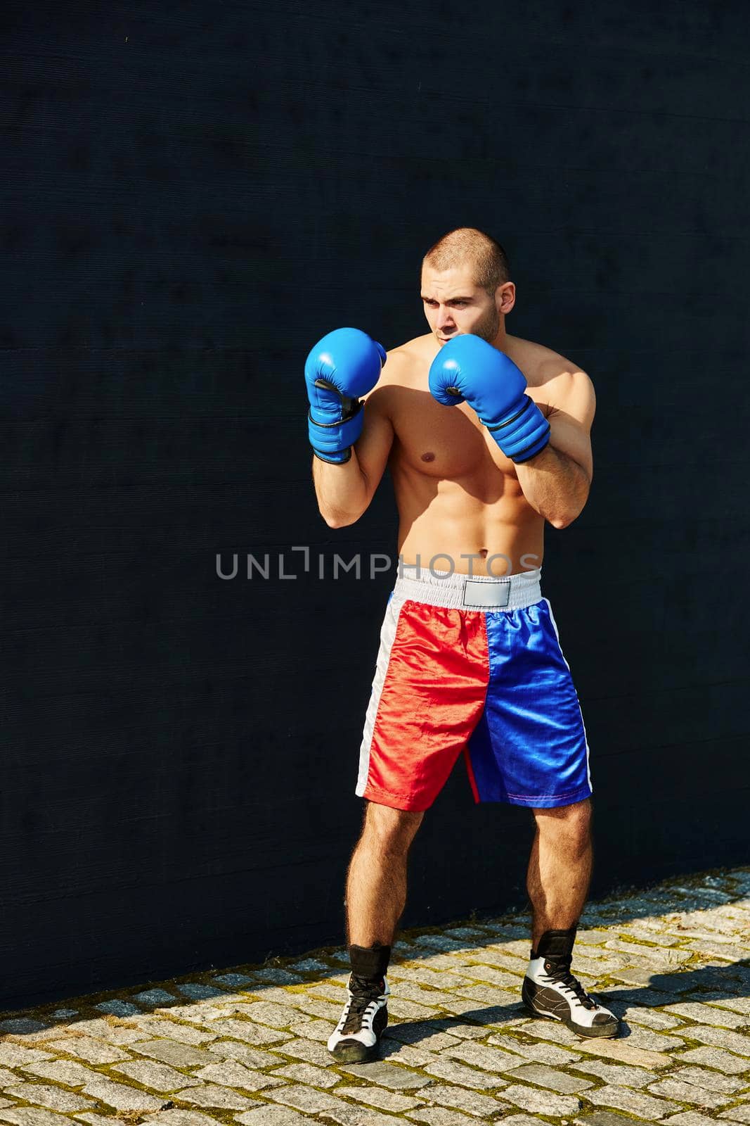 Boxer in multi-colored sports shorts and gloves practicing on the street.