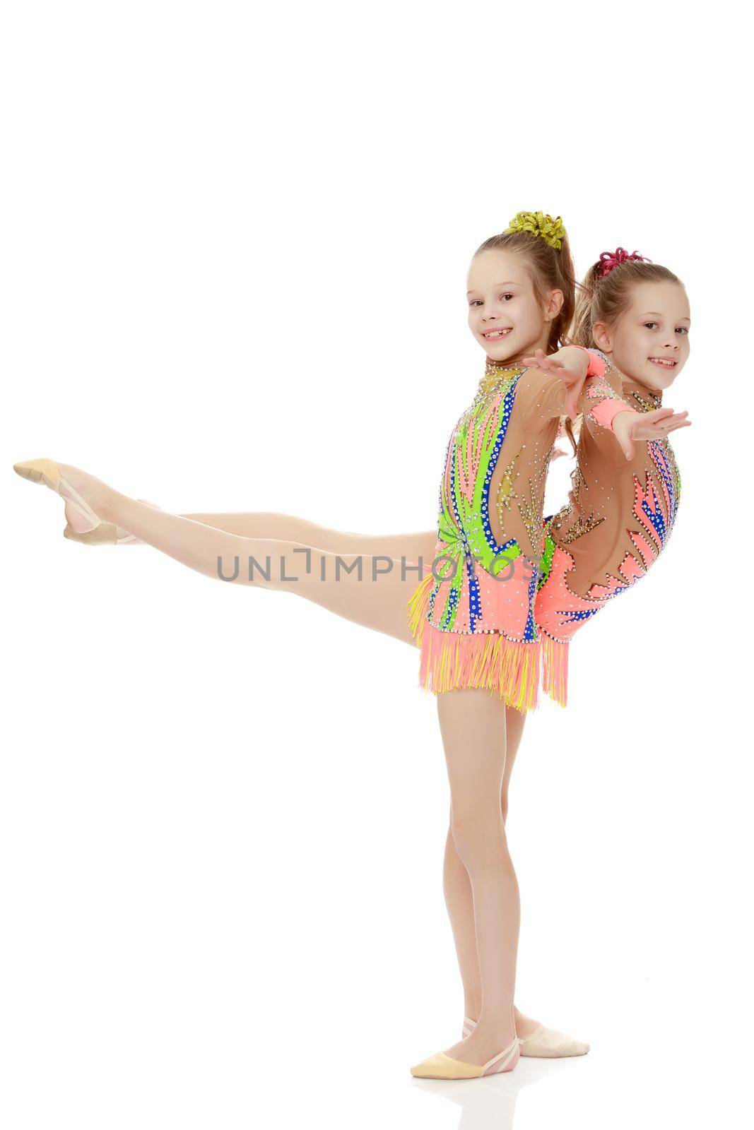 Two adorable little twin girls, gymnastics in the sports school. Girls beautiful gymnastic leotards. They do the splits.Isolated on white background.