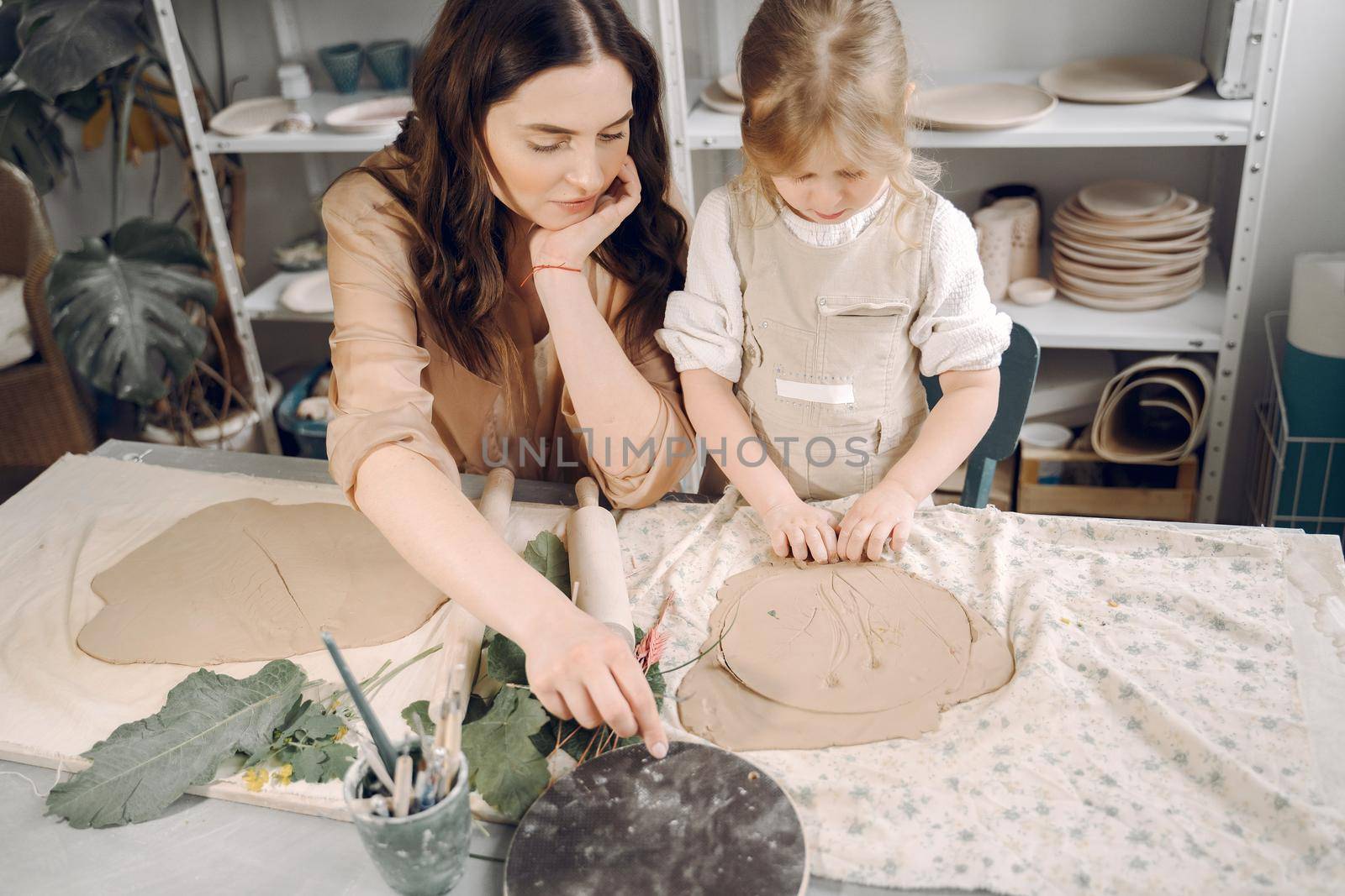 Woman and girl kneading clay. Family make art product at table in pottery workshop. Mother with daughter.