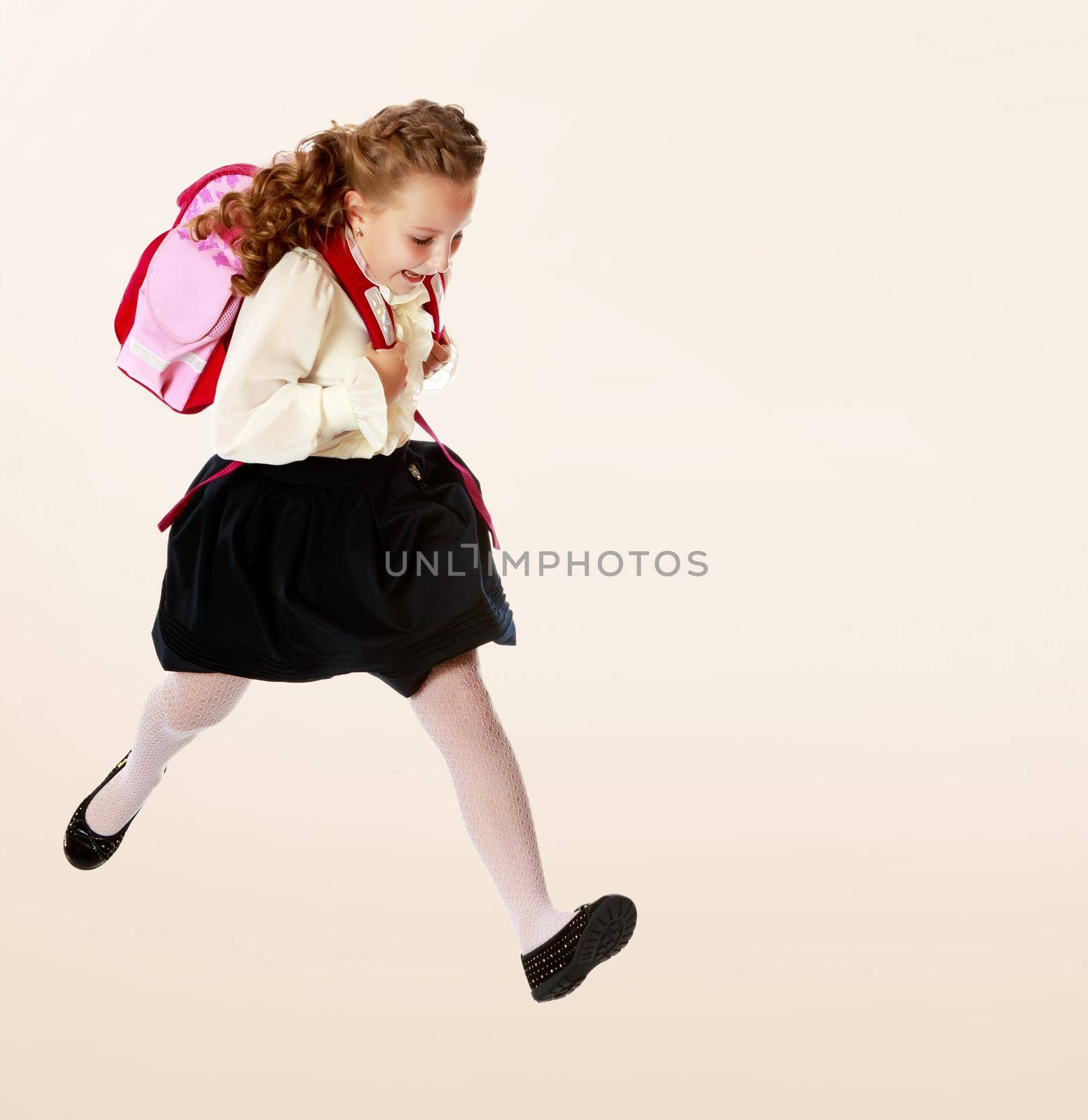 Pretty little girl schoolgirl in white blouse and black skirt to hurry to school. She jumps over the obstacle.On a brown gradient background.