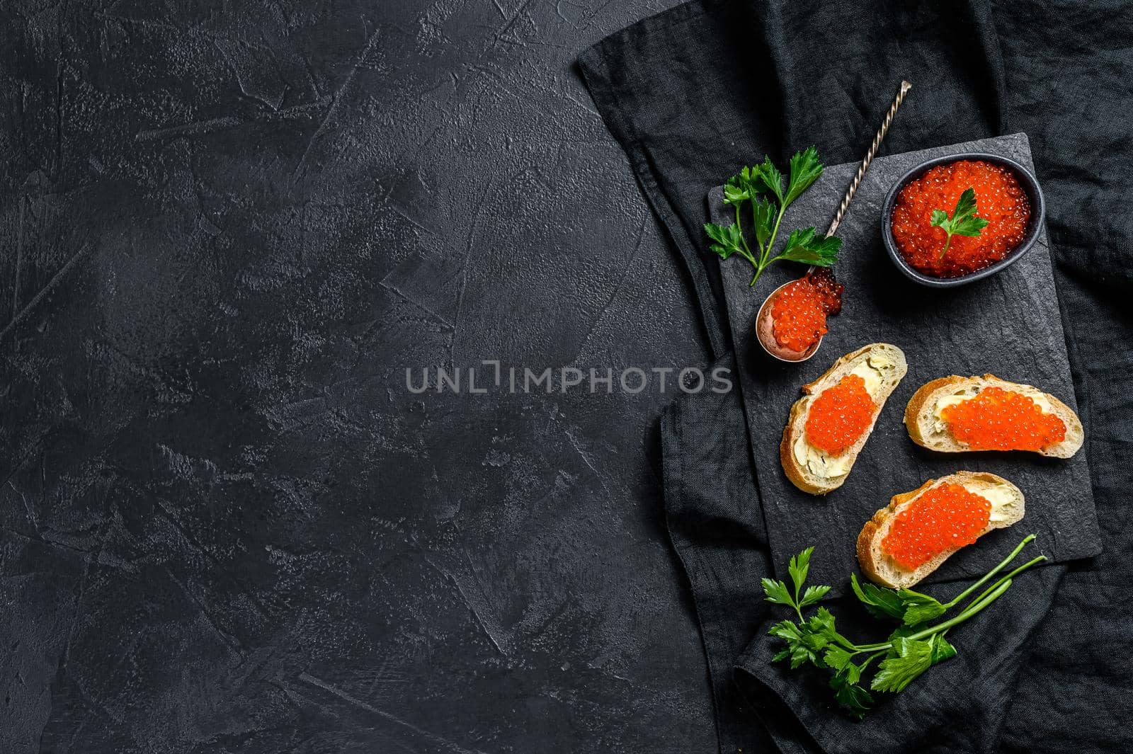 Red caviar in bowl and Sandwiches on stone board. Black background. Top view. Copy space.