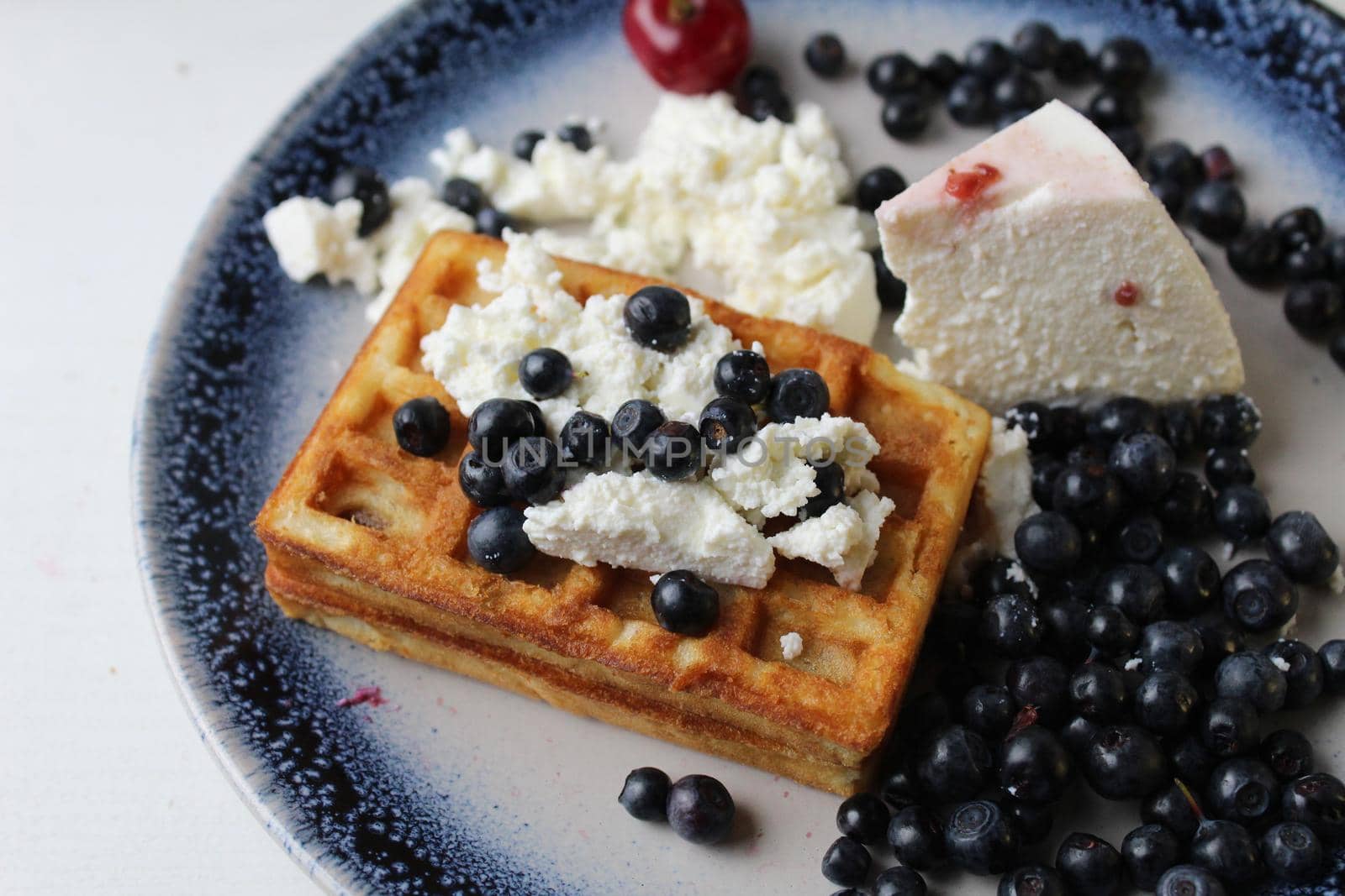 delicious healthy breakfast. Belgian soft waffles with curd cheese cream and blueberry cherries lie white blue plate view from the top. Delicious still life by Shoba