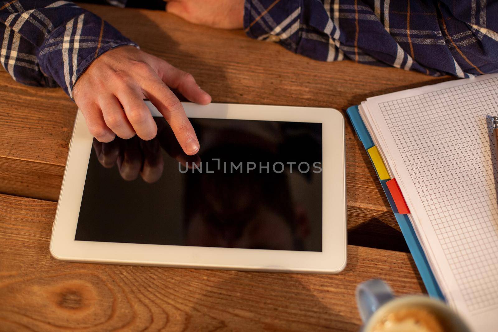 Cropped image of man using tablet works. White tablet with blank screen in a man hands on table at coffee shop or home office, working from cafe concept