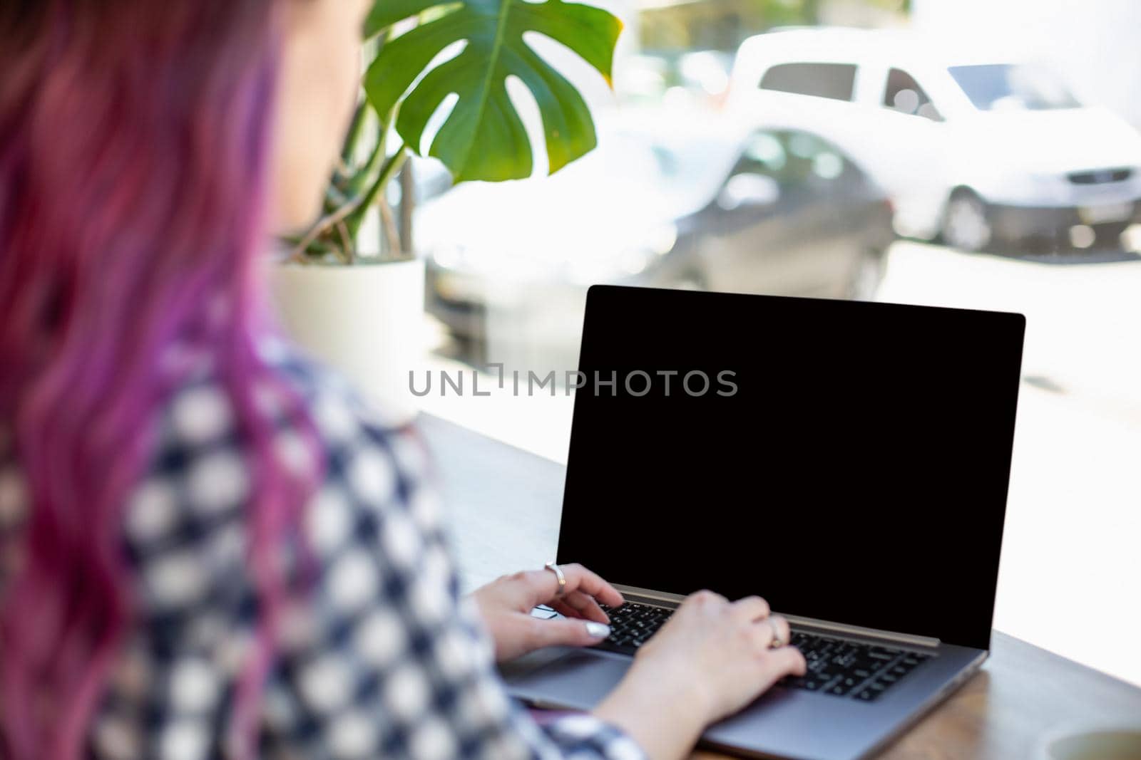 Back view of a young pink hair woman keyboarding on laptop computer with blank copy space screen while sitting in cafe. by nazarovsergey