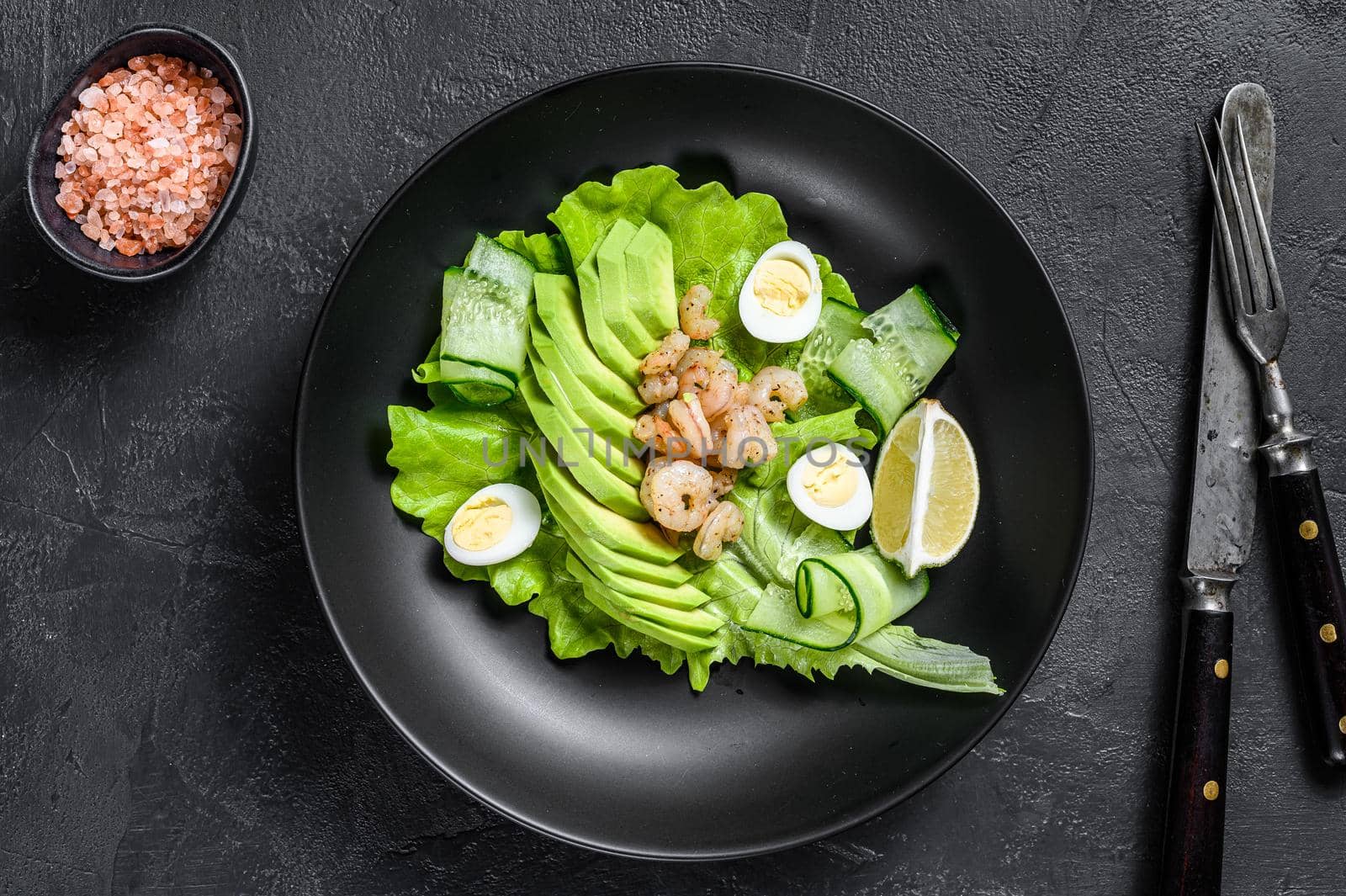 Fresh seafood salad with grilled shrimps prawns, egg, avocado and cucumber in a plate. Black background. top view.