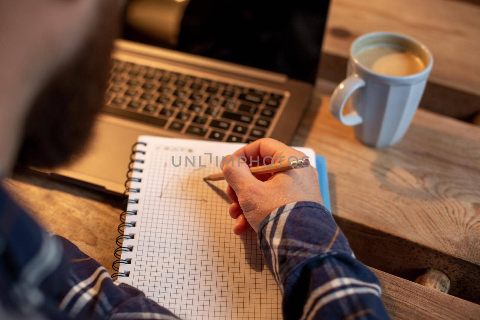 Cropped image of casual business man or freelancer planning his work on notebook, working on laptop computer with smart phone, cup of coffee on table at coffee shop or home office, working from cafe concept