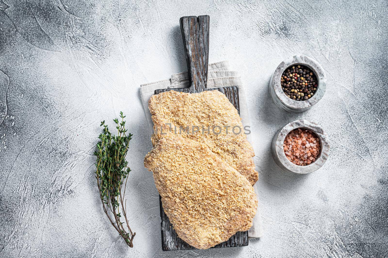 Wiener Raw schnitzel in breadcrumbs on wooden board. White background. Top view by Composter