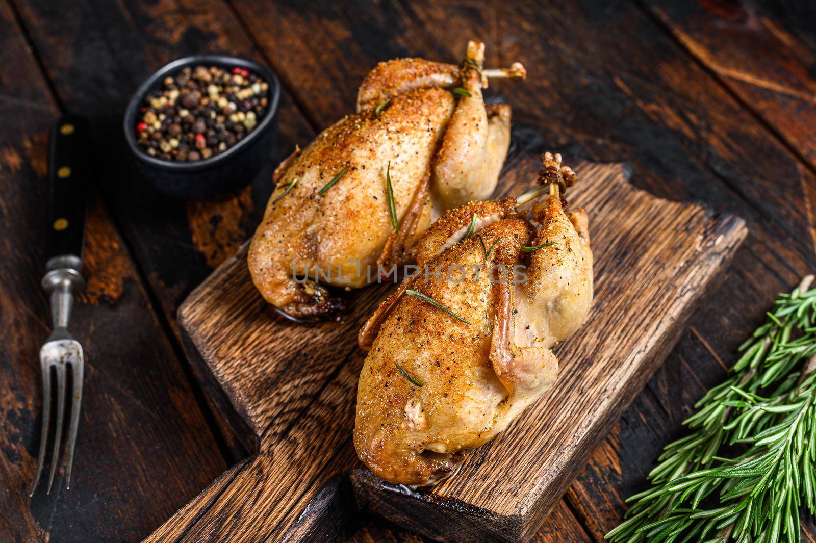 Homemade baked quail on a cutting board. Dark Wooden background. Top view by Composter