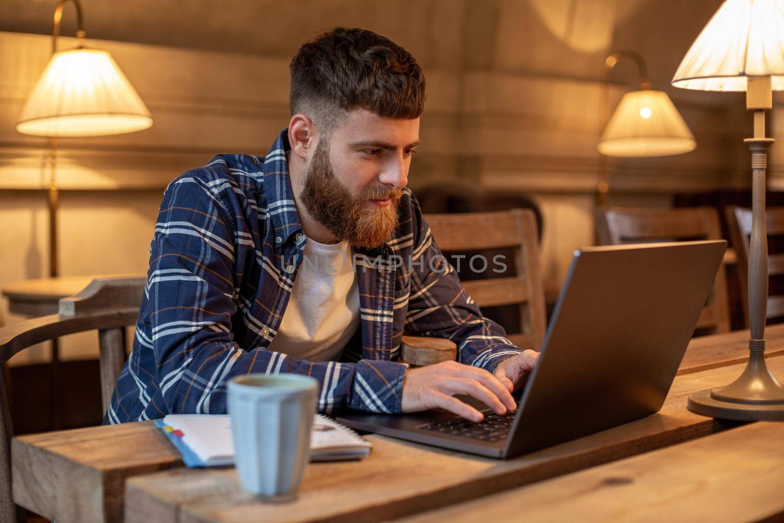 Young professional surfing the Internet on his laptop with cup of coffee on table at coffee shop or home office, working from cafe concept
