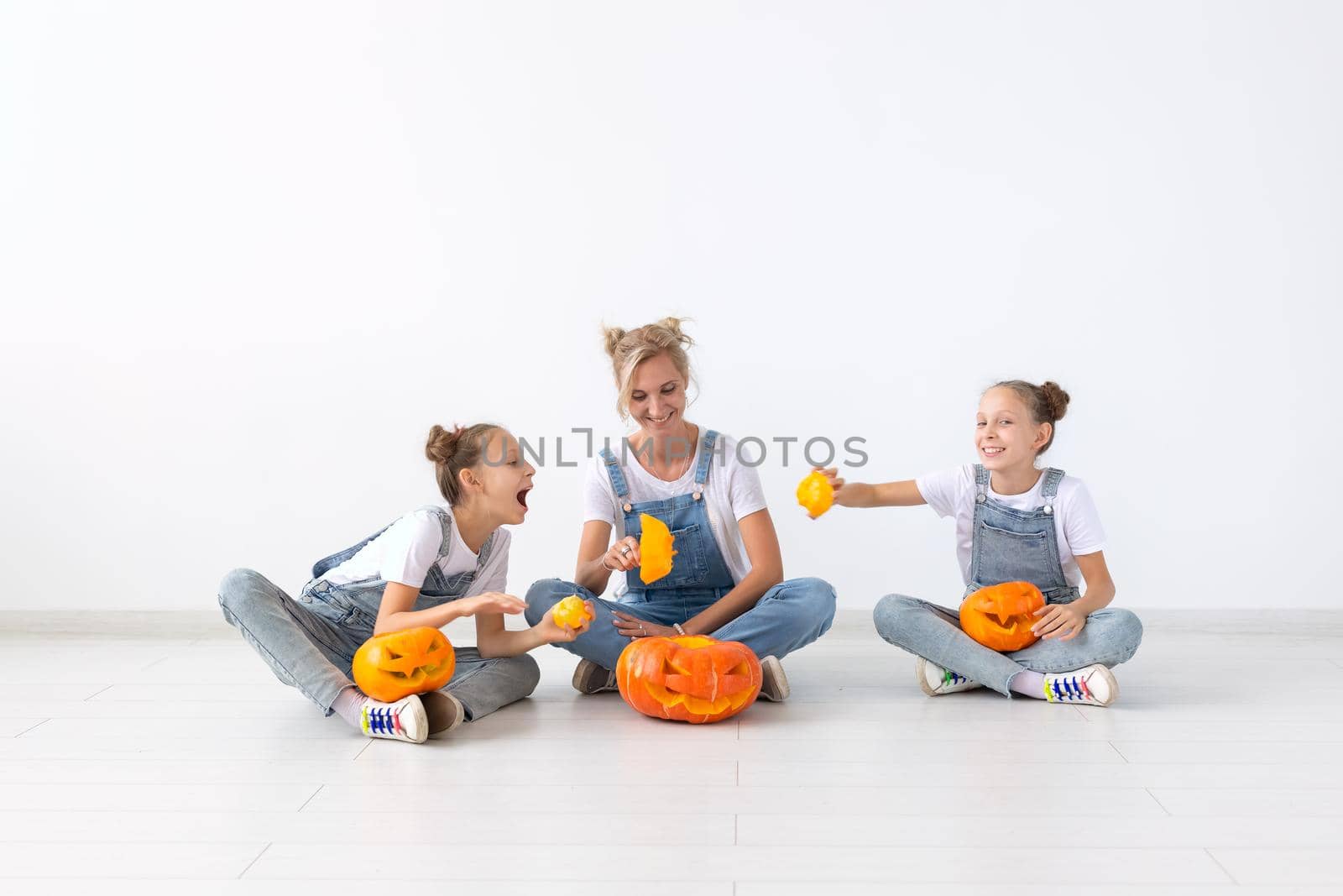 Happy halloween and holidays concept - A mother and her daughters with pumpkins. Happy family preparing for Halloween. by Satura86