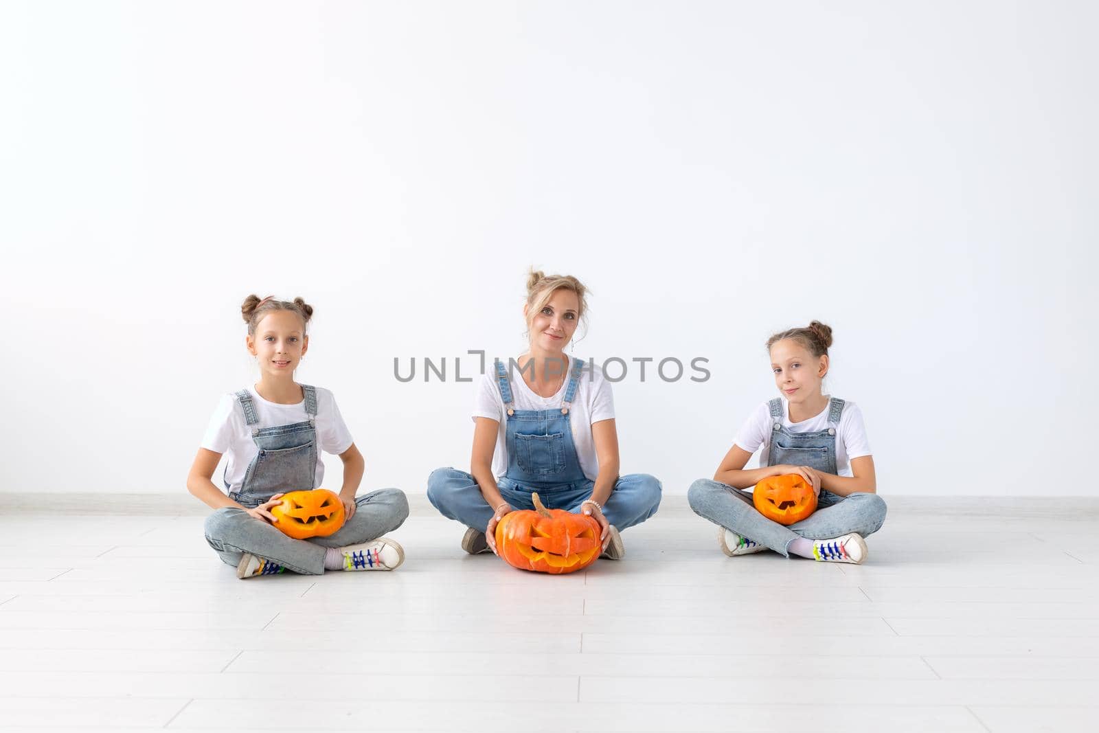 Happy halloween and holidays concept - A mother and her daughters with pumpkins. Happy family preparing for Halloween. by Satura86