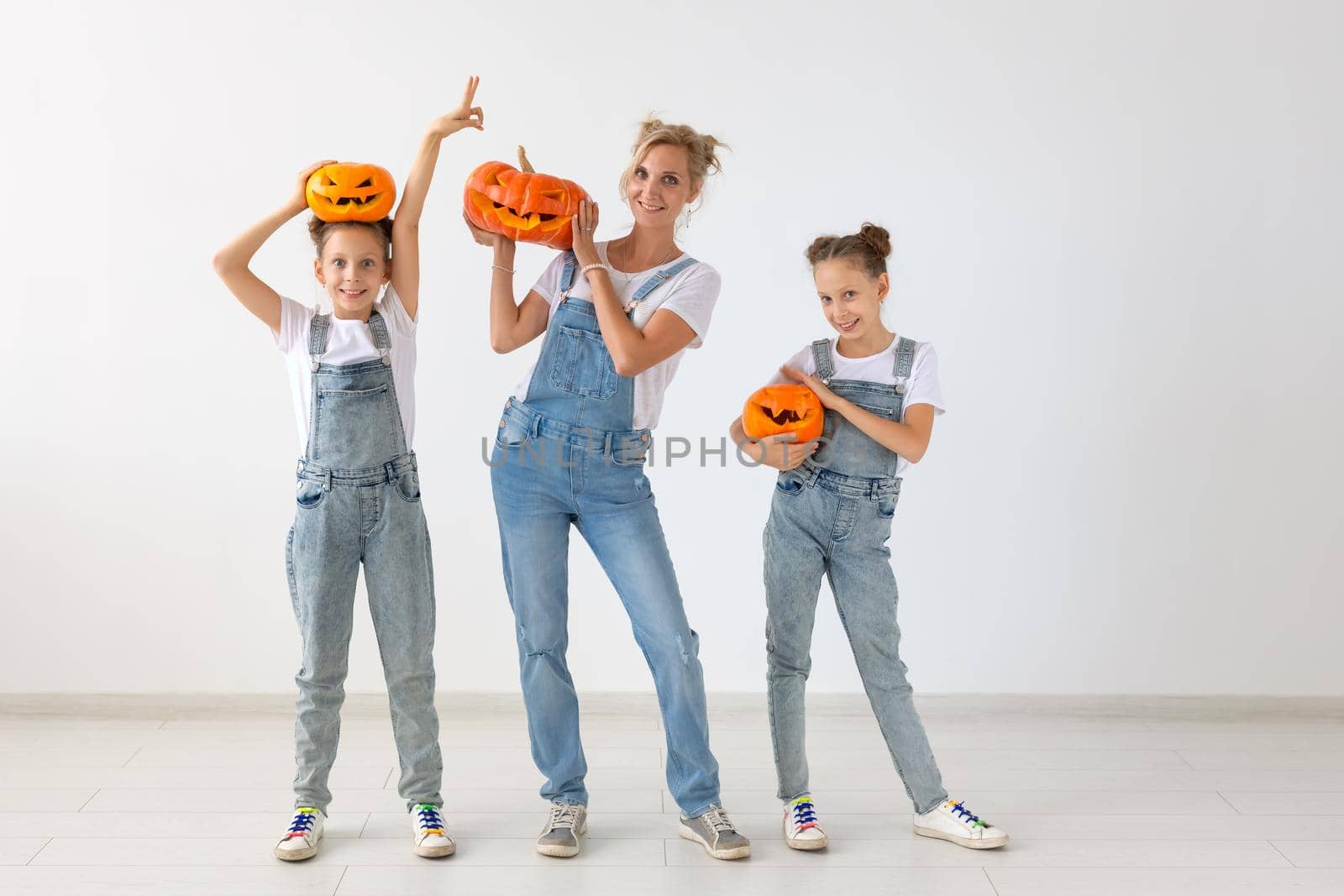 Happy halloween and holidays concept - A mother and her daughters with pumpkins. Happy family preparing for Halloween