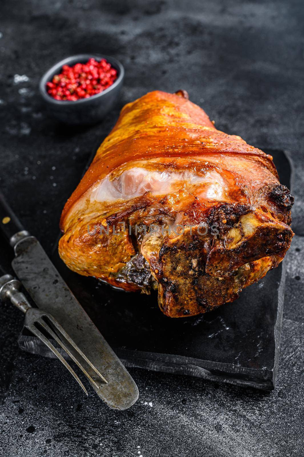 Roast pork knuckle with pink pepper and spices. Black background. Top view by Composter