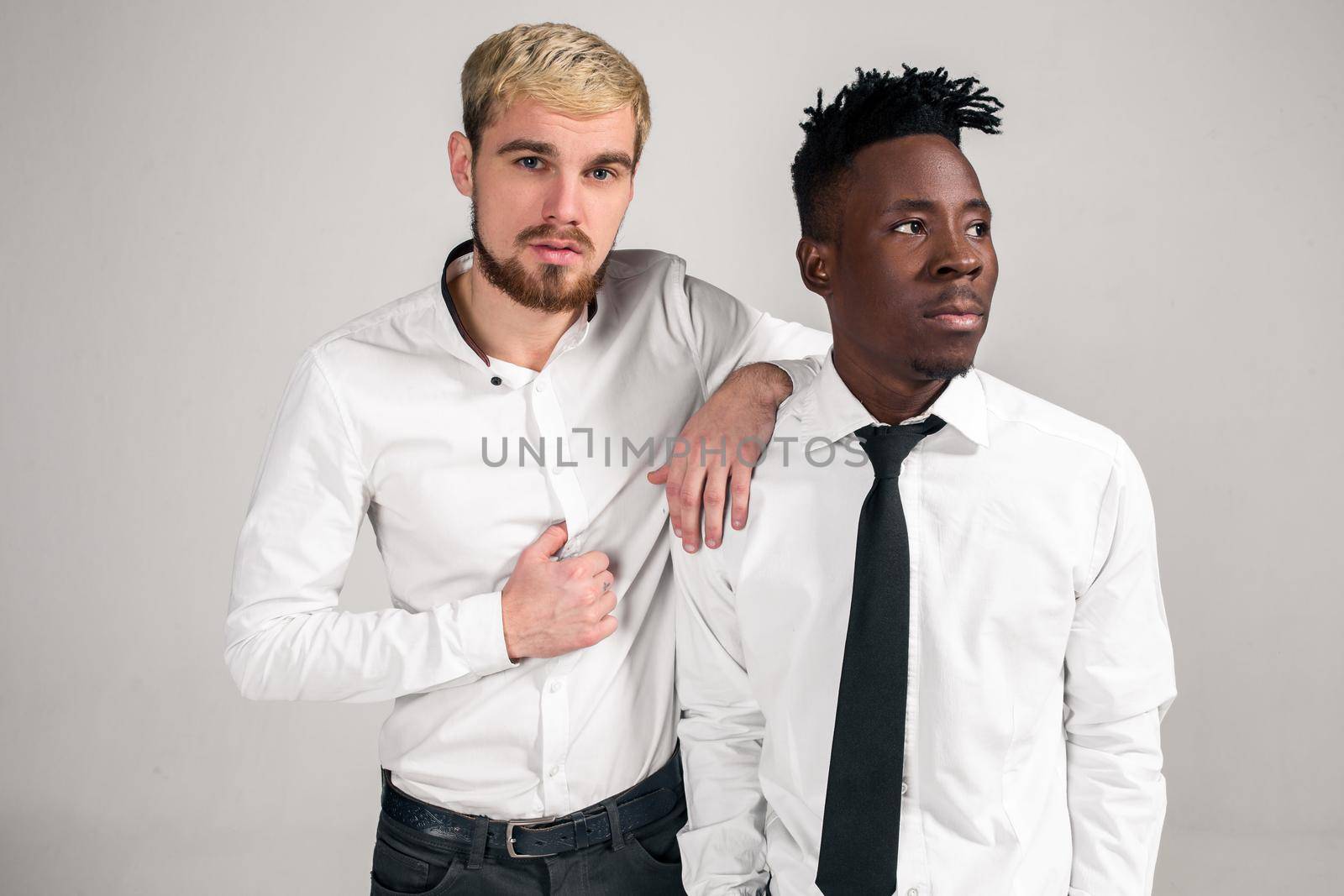 Two stylish men posing and having fun on white background. Friends. Two guys in white shirts and dark pants at studio