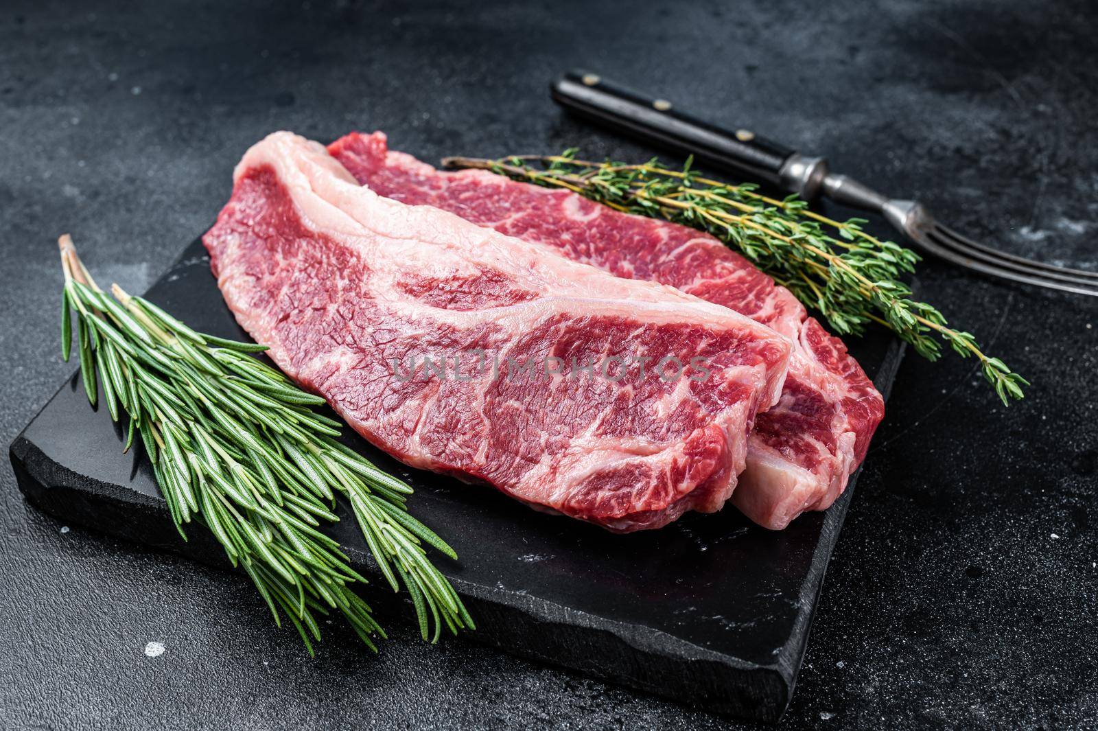 Raw Striploin steak or New York steak beef meat cut. Black background. Top view.