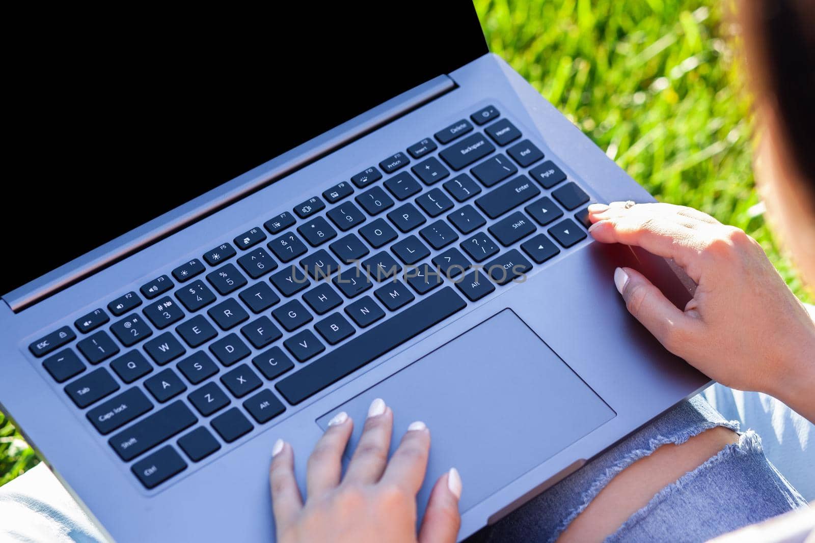 Close up hands on keyboard. Woman working on laptop pc computer with blank black empty screen to copy space in park on green grass sunshine lawn outdoors. Mobile Office. Freelance business concept