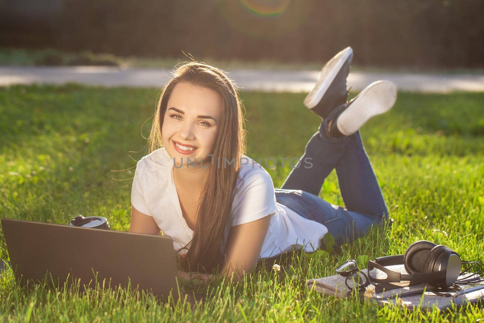 Young woman using laptop in the park lying on the green grass. Modern lifestyle, information technology or online shopping concept