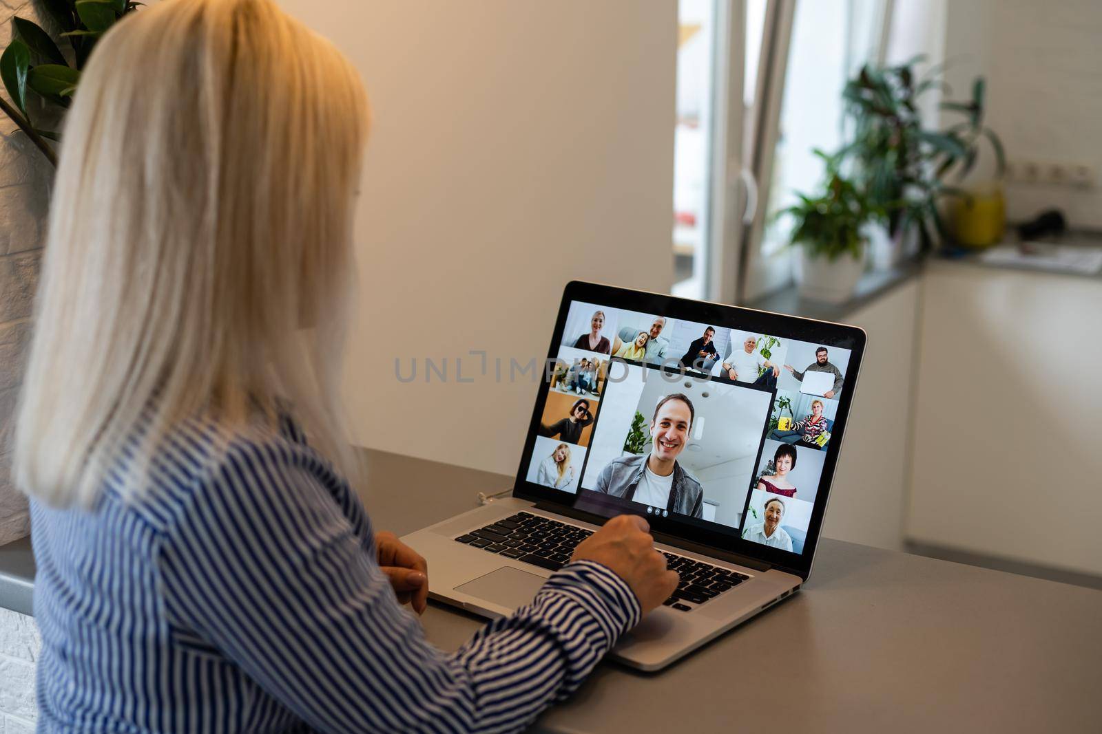 Back view of business woman talking to her colleagues about plan in video conference. Multiethnic business team using laptop for a online meeting in video call. Group of people smart working from home by Andelov13