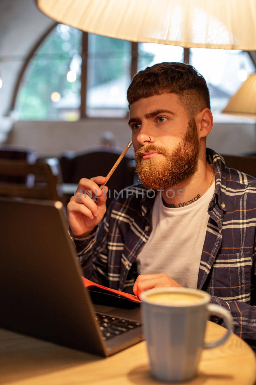Casual business man or freelancer planning his work on notebook, working on laptop computer with smart phone, cup of coffee on table at coffee shop or home office, working from cafe concept