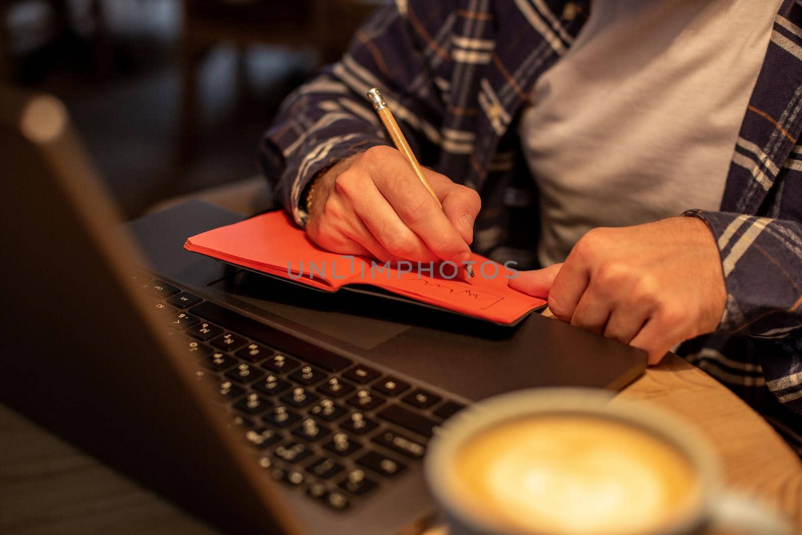 Cropped image of casual business man or freelancer planning his work on notebook, working on laptop computer with smart phone, cup of coffee on table at coffee shop or home office, working from cafe concept