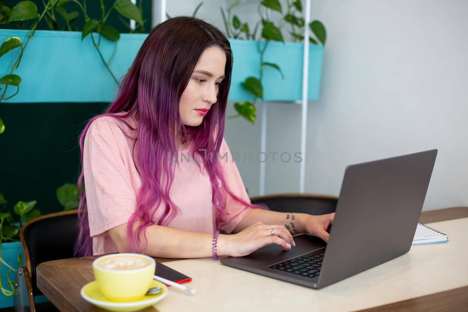 Young woman with pink hair with laptop computer sitting in cafe, intelligent female student working on net-book. by nazarovsergey