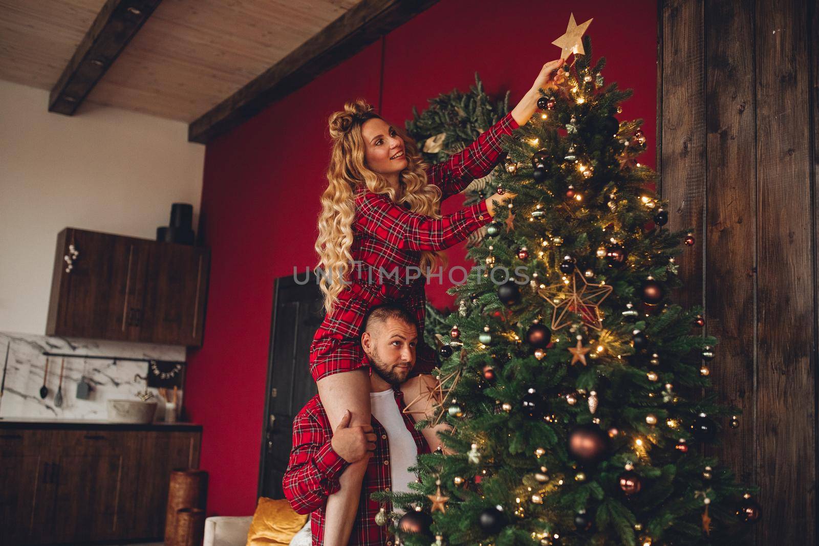 Cheerful couple in love in the same sleepwear decorates christmas tree together at home by StudioLucky