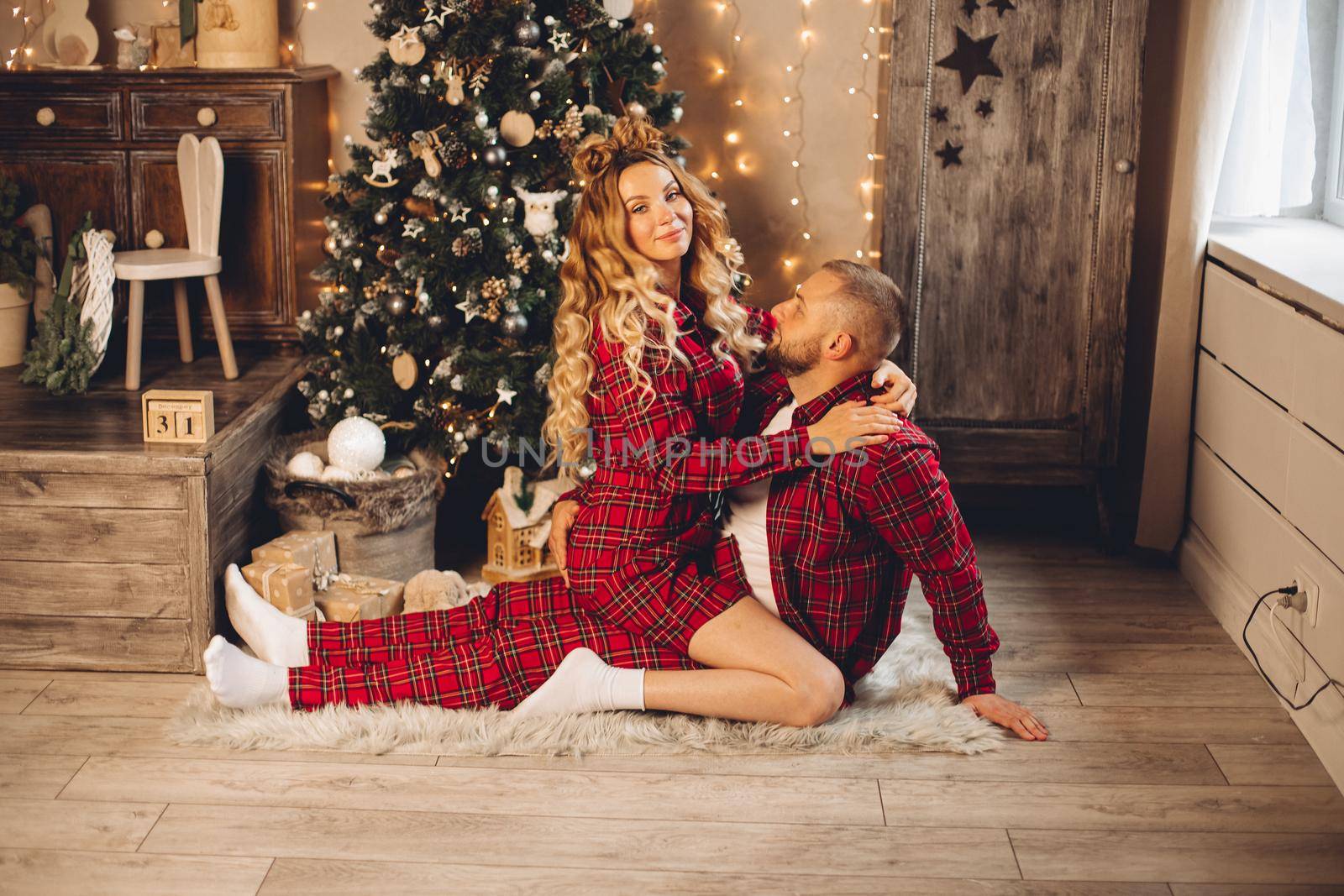 Happy couple in love sitting next to Christmas tree on the floor of a house. Holiday concept