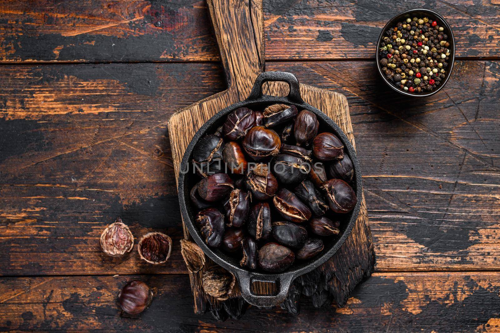 Roasted chestnuts served in a pan on a wooden cutting board. Wooden background. Top view by Composter