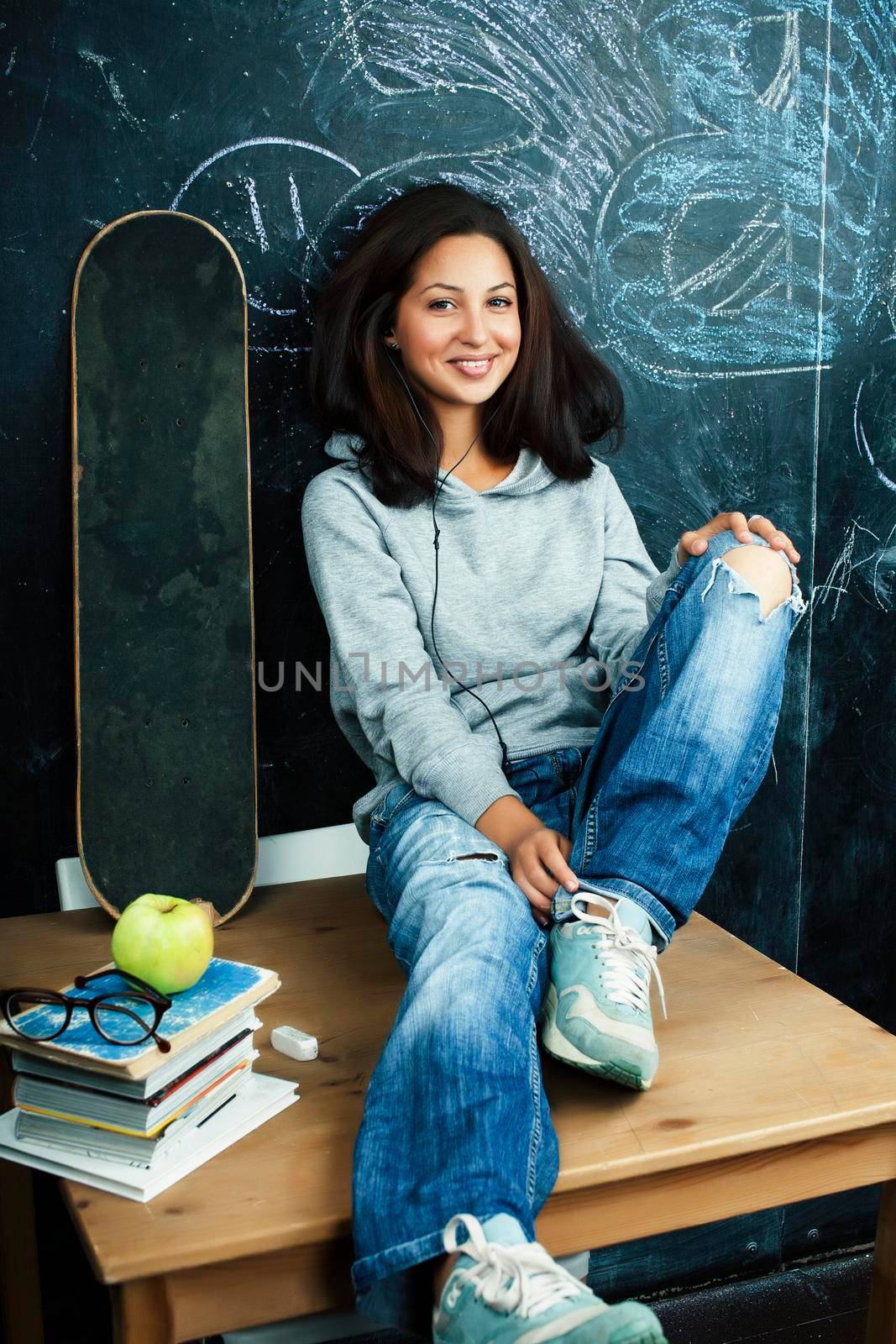 young cute teenage girl in classroom at blackboard seating on table smiling, modern hipster concept by JordanJ