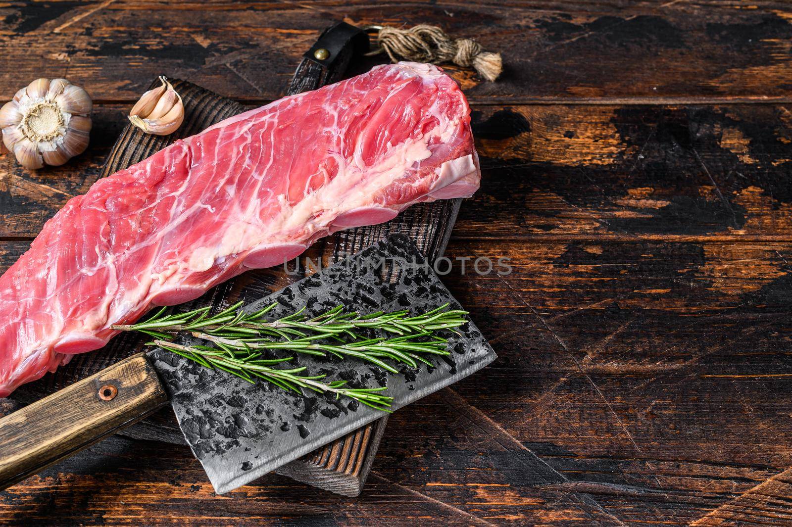 Raw veal brisket meat on short spare rib with butcher knife. Dark wooden background. Top view. Copy space.