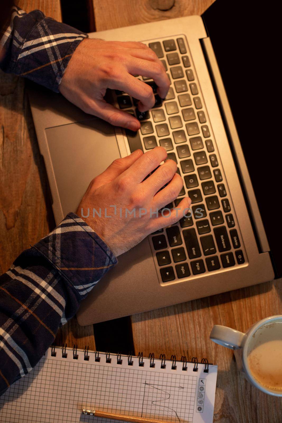 Young man drinking coffee in cafe and using laptop. Man's hands using laptop during coffee break. Working from cafe concept