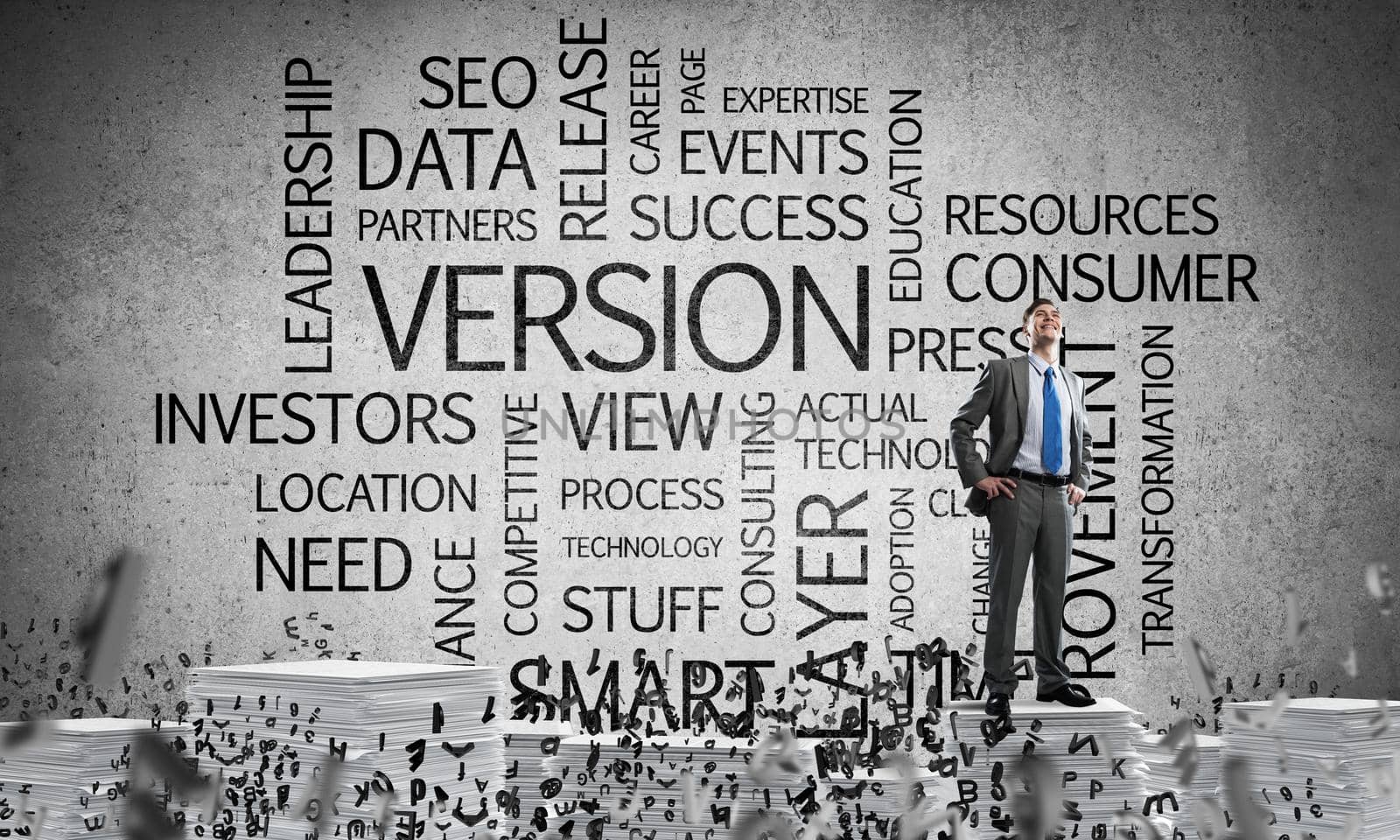 Confident businessman in suit standing on pile of documents among flying letters with business related terms on background. Mixed media.
