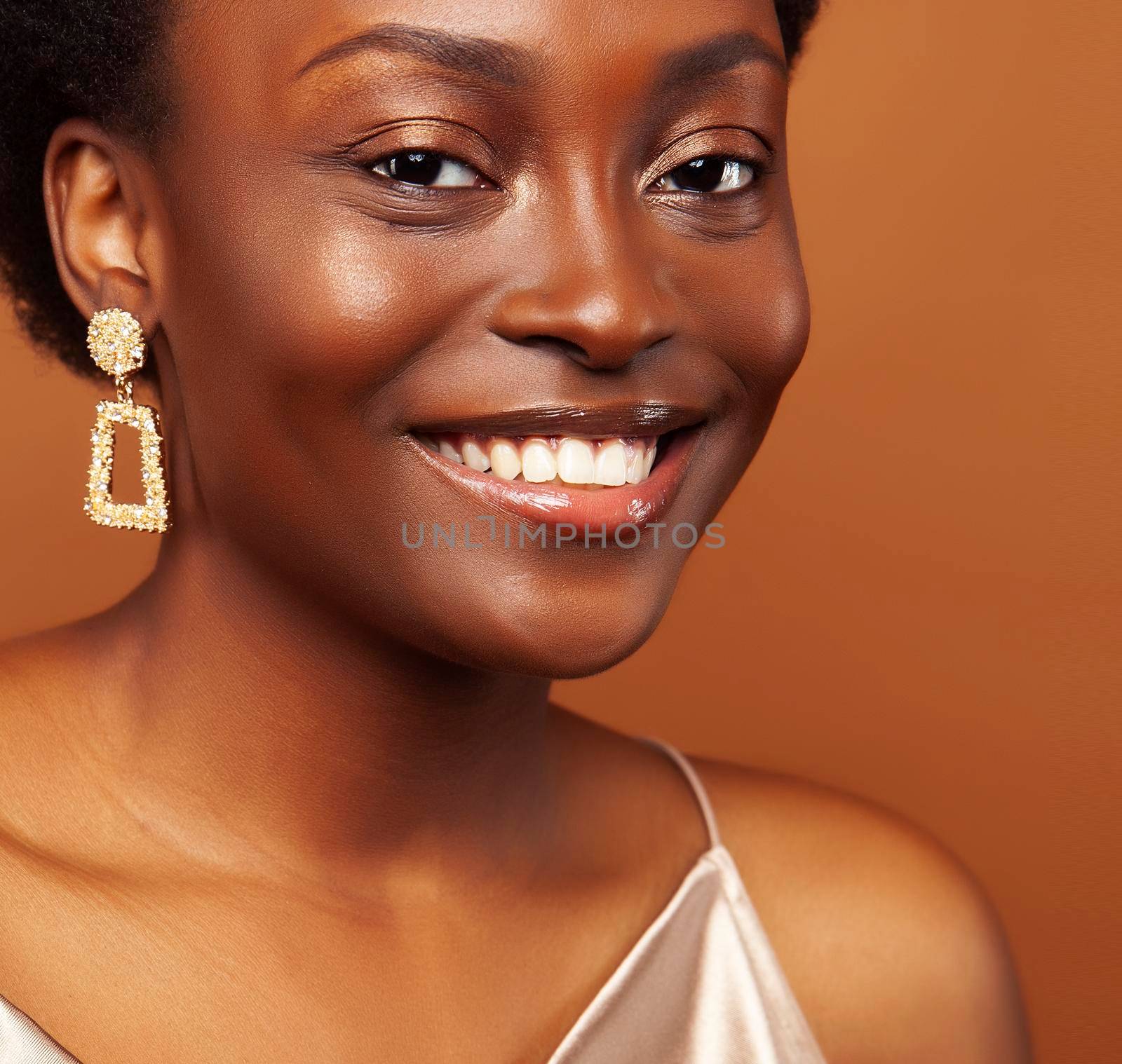 pretty young african american woman with curly hair posing cheerful gesturing on brown background, lifestyle people concept close up