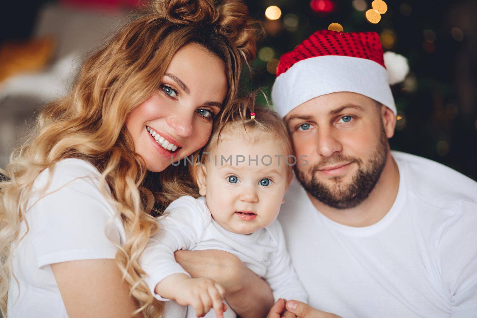 Beautiful smiling mother and father in Santa hat embracing their daughter. Christmas time.