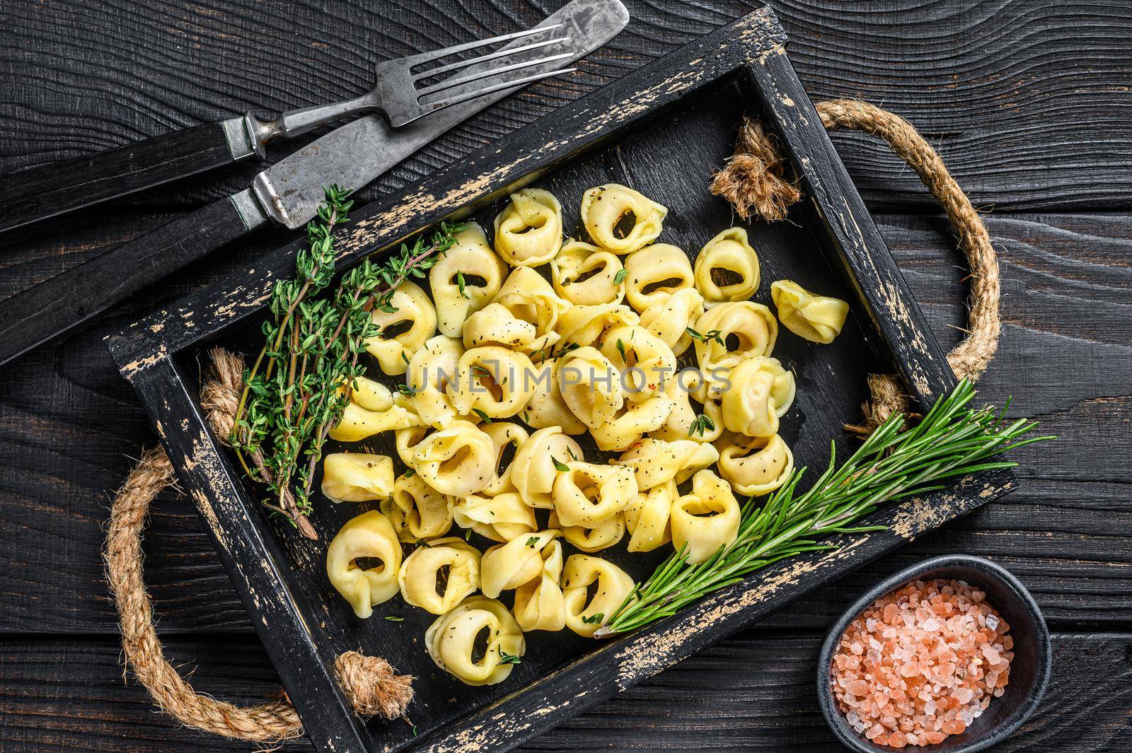 Italian traditional tortellini pasta with spinach in a wooden tray. Black wooden background. Top view.