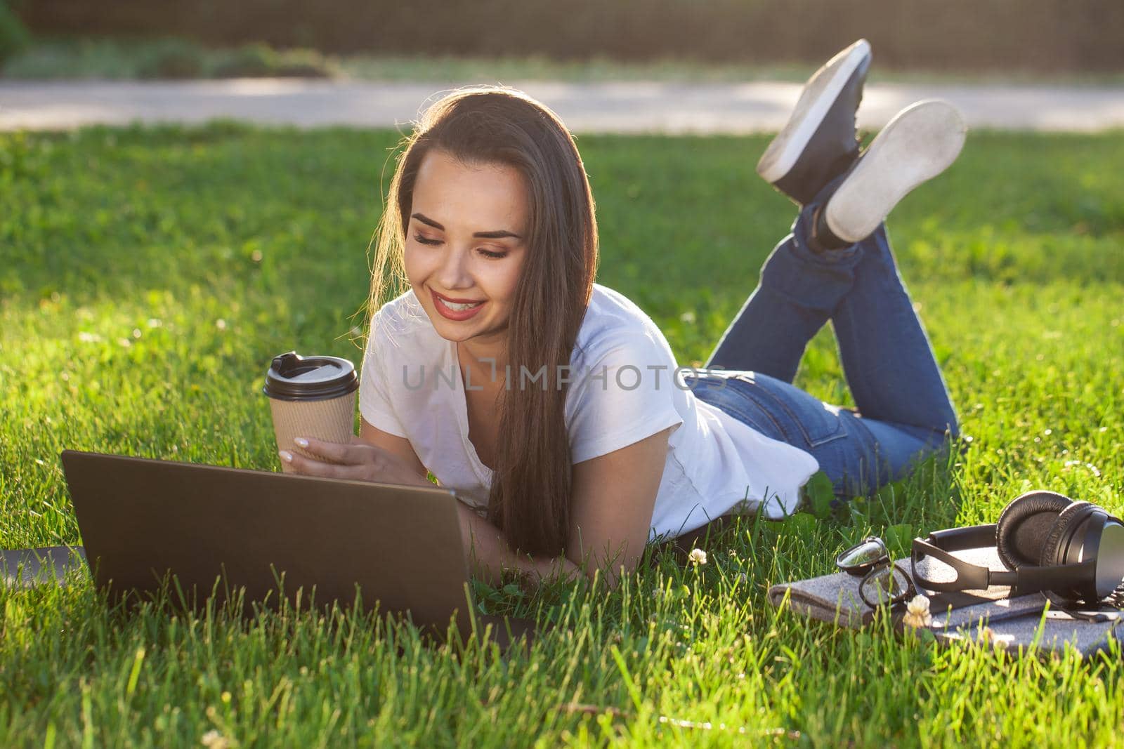Young woman using laptop in the park lying on the green grass. Modern lifestyle, information technology or online shopping concept