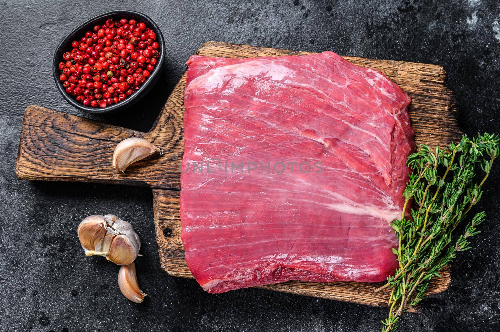Raw flank or flap beef meat steak on a wooden cutting board. Black background. Top view by Composter