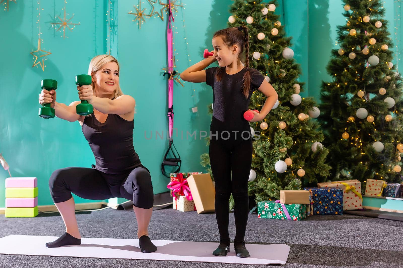 mother and daughter doing fitness near the christmas tree at gym. New Year. Christmas, holidays, fitness, and gym concept. by Andelov13