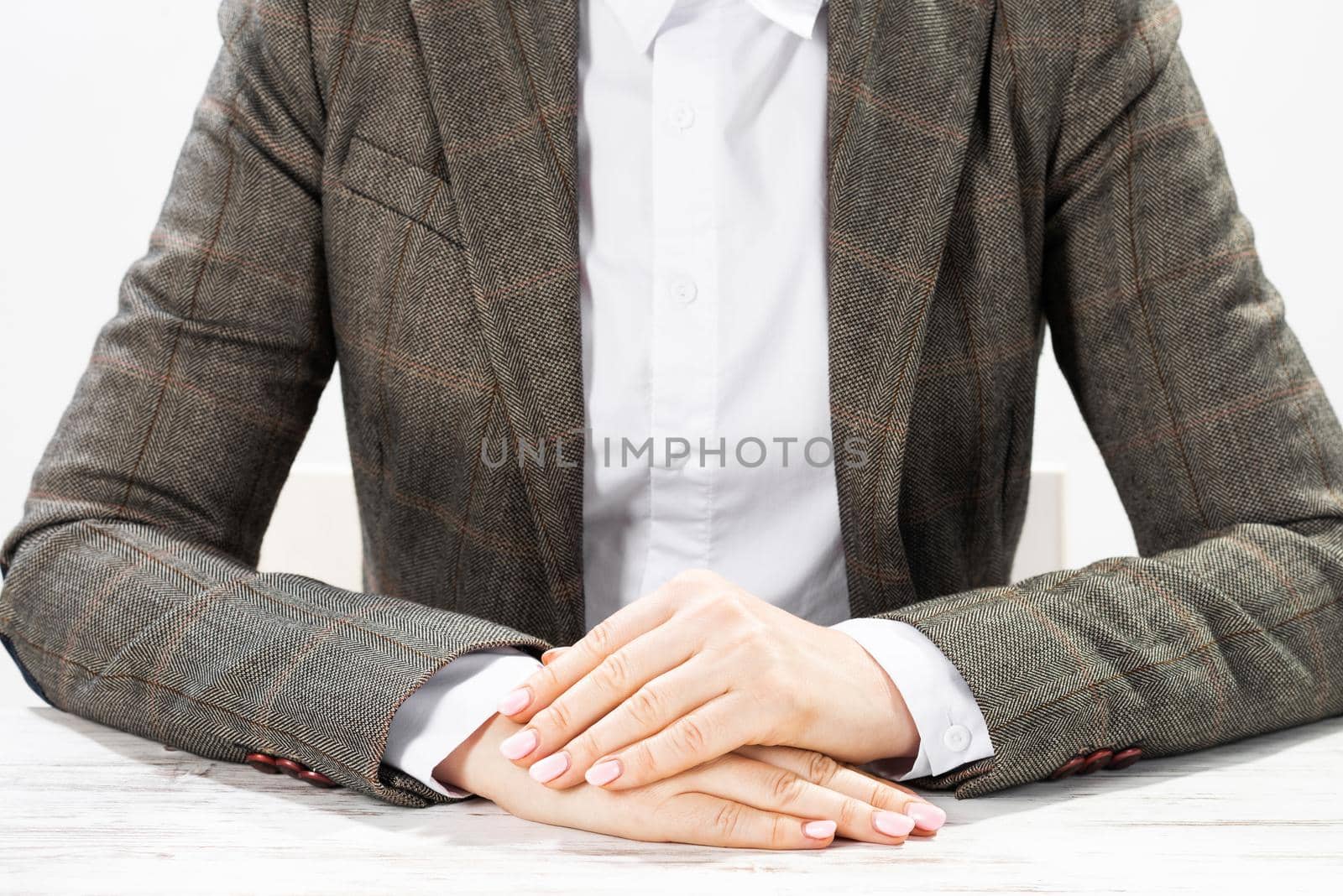 Close up businesswoman sitting at desk with folded arms. Concentrated business lady on background of white wall. Business consultation in office. Corporate woman in suit posing at her workplace.