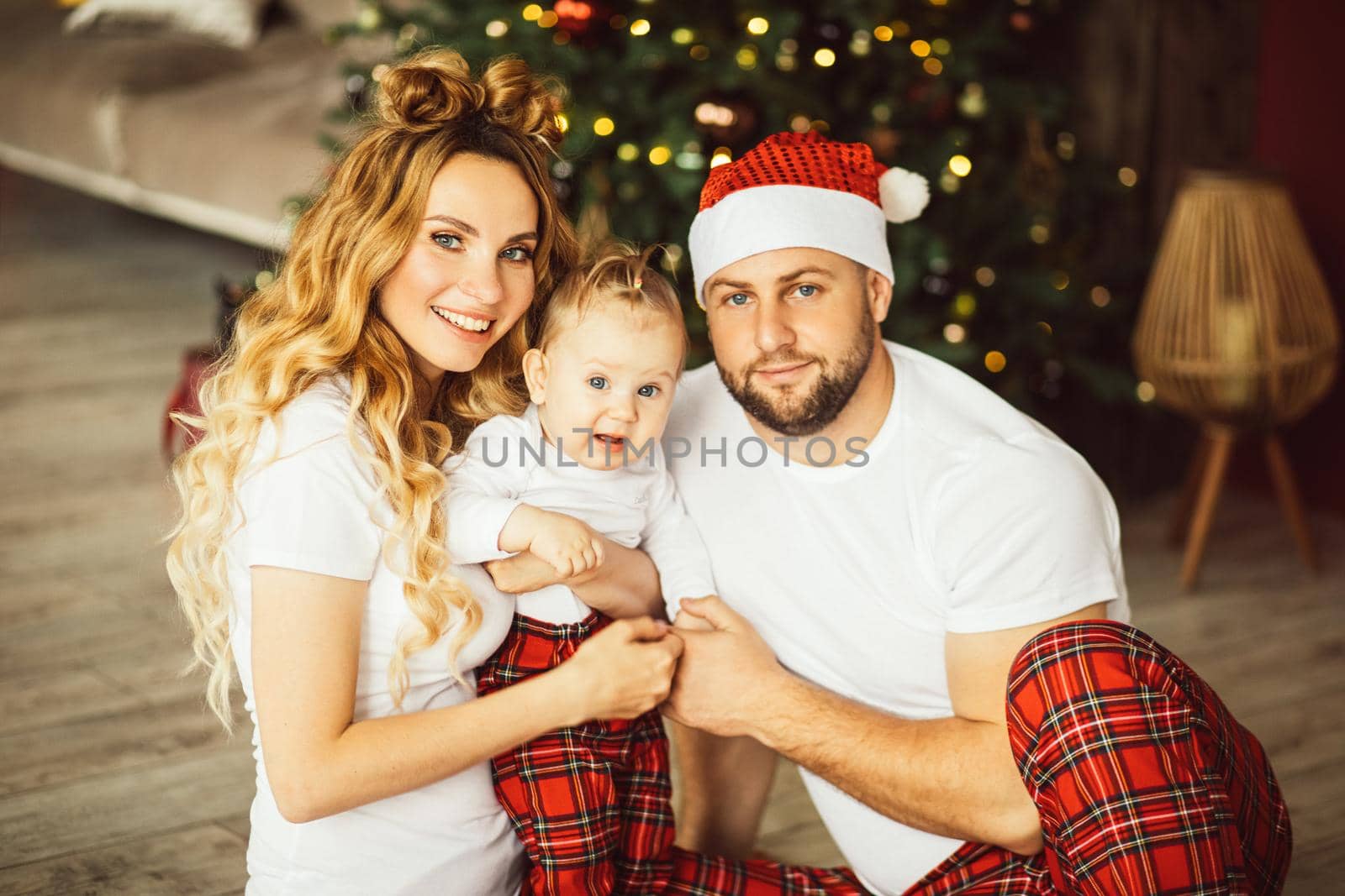 Waist up of smiling couple and cute kid sitting on floor with Christmas tree on the background