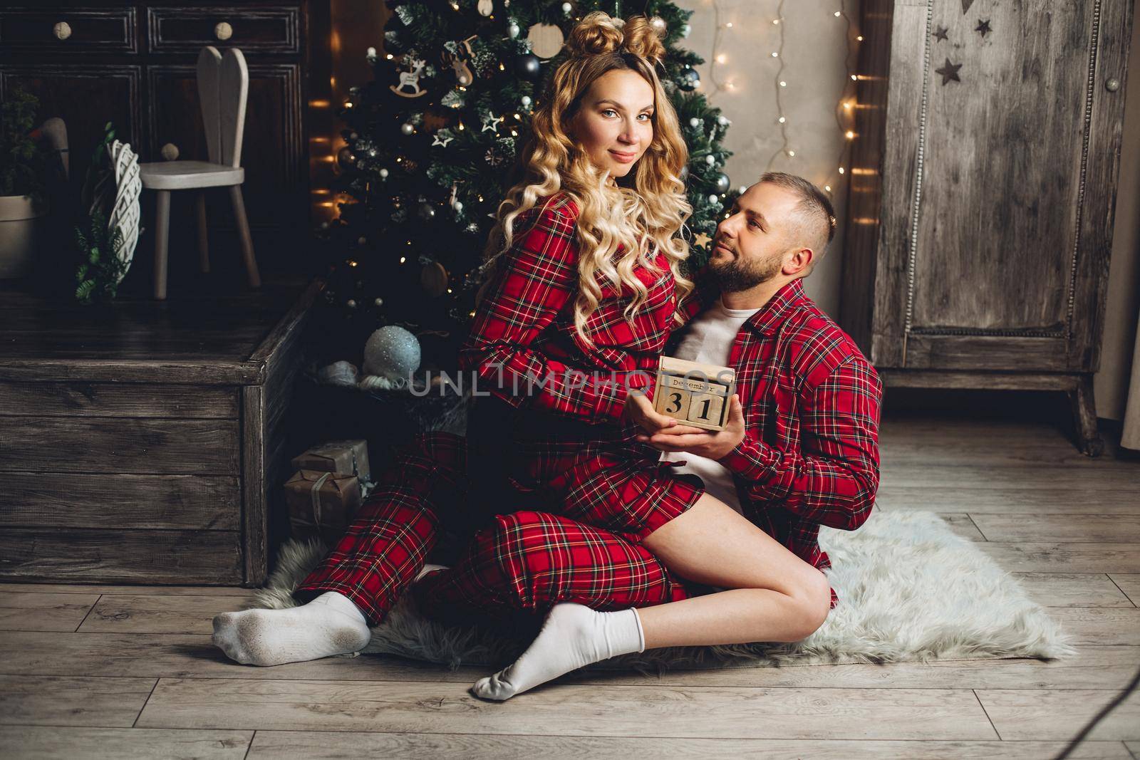 Smiling young man looking at his girlfriend with a Christmas tree in the background by StudioLucky