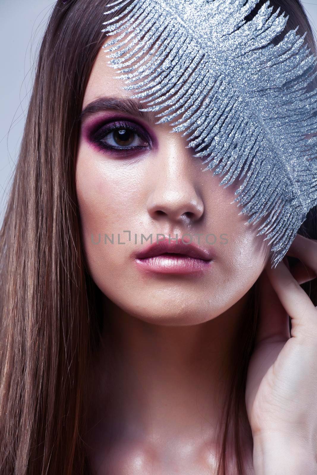 beauty brunette young girl with fashion makeup and silver feather close up on white background