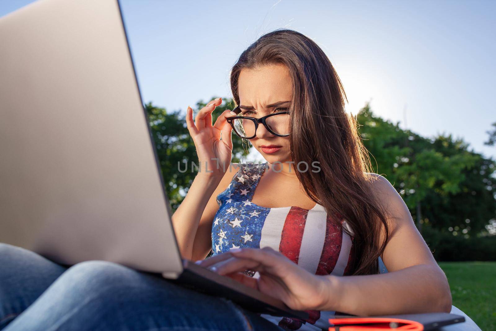 Pretty young woman sitting on bean bag use laptop while resting on grass in park on the sun. Success small business, modern lifestyle, information technology, or online shopping concept