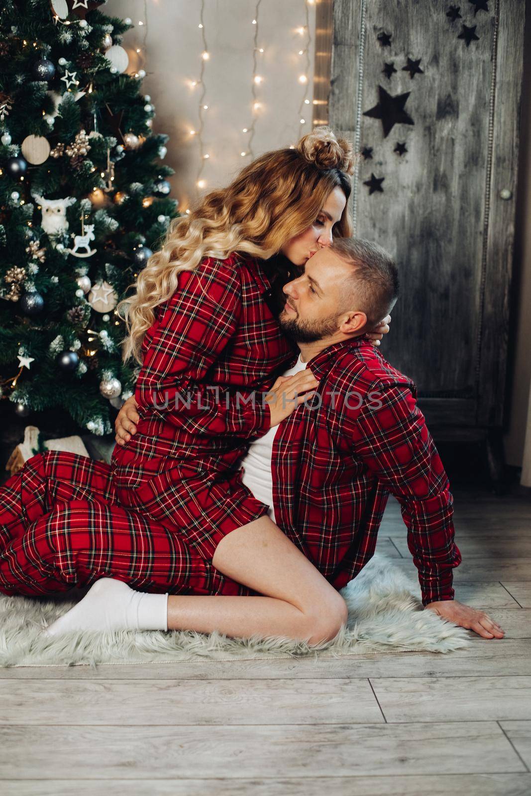 Woman kissing her boyfriend by xmas tree. by StudioLucky