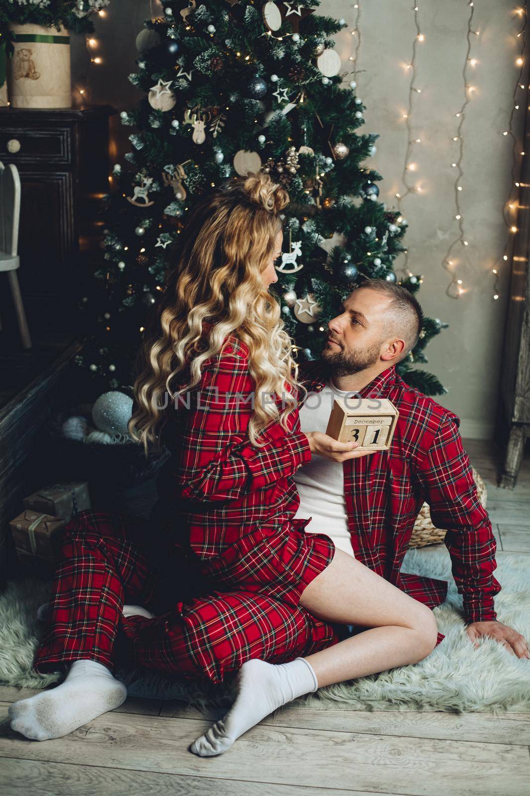 Couple in love wearing matching pajamas while sitting on floor near Christmas tree at home