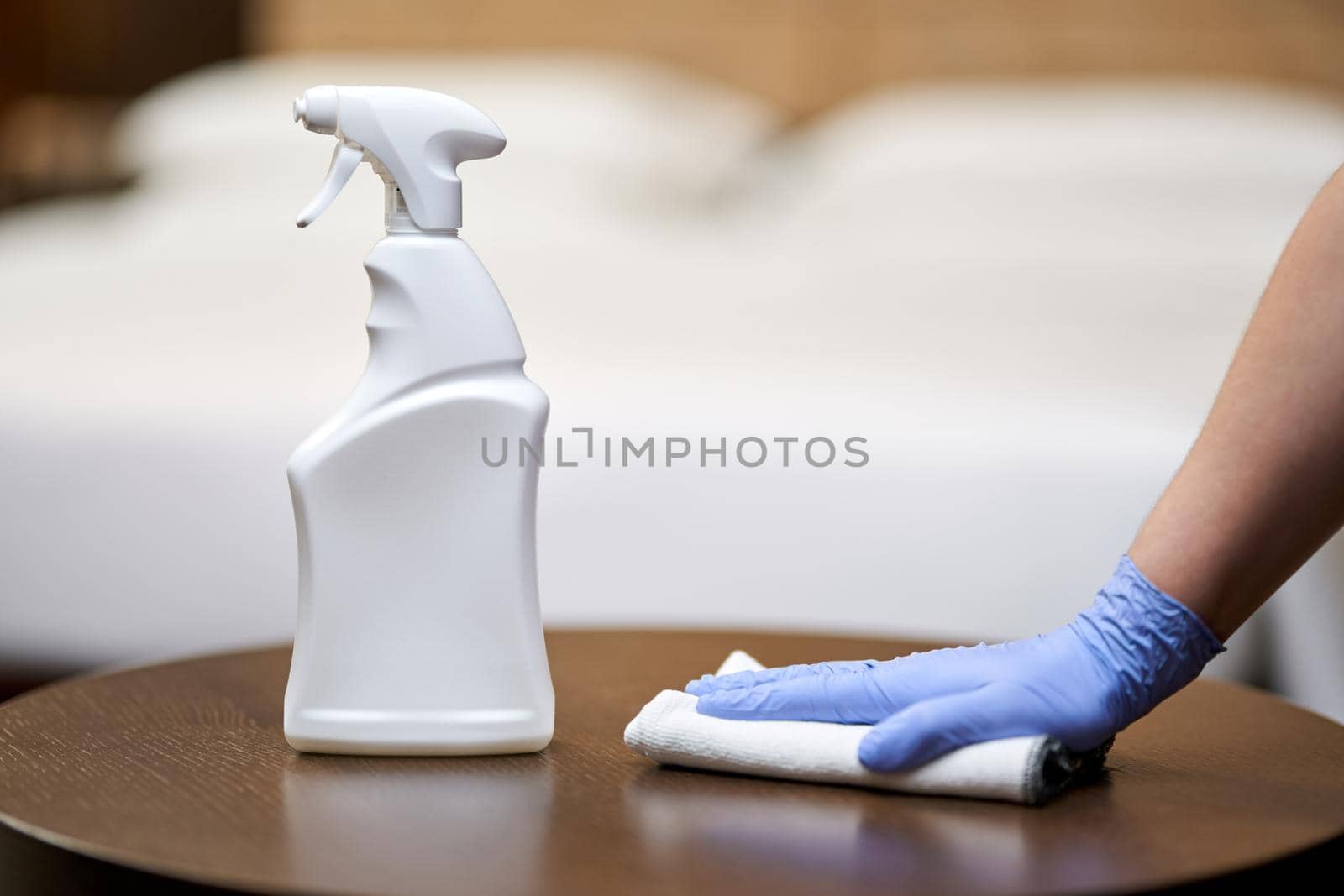 Close up of chambermaid cleaning and polishing wooden table with a spray detergent in hotel room. Housekeeping and hygiene concept