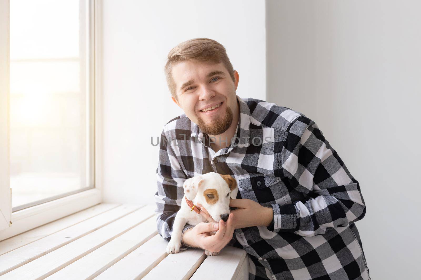 people, pets and animals concept - young man hugging puppy near window on white background by Satura86