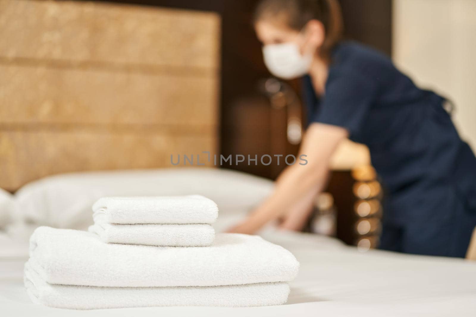 White fresh towels on the bed with a maid in a mask on the background. Hotel service concept