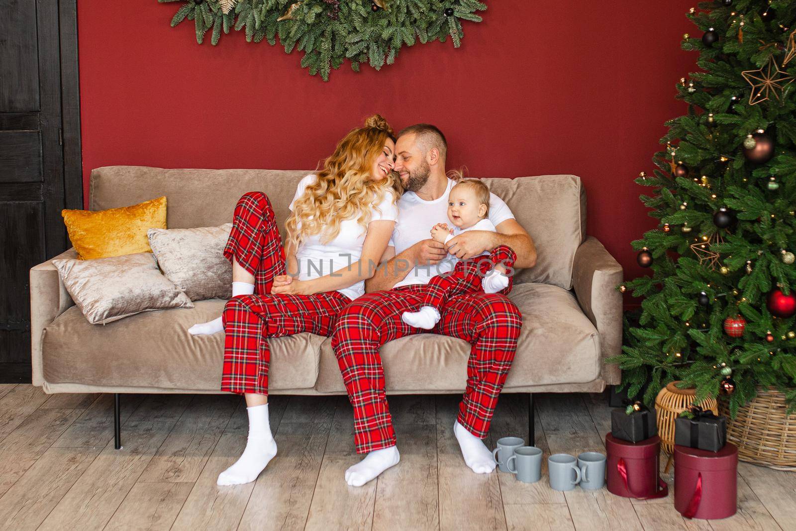 Happy parents and their baby sitting on sofa near Christmas tree at home. Holiday concept