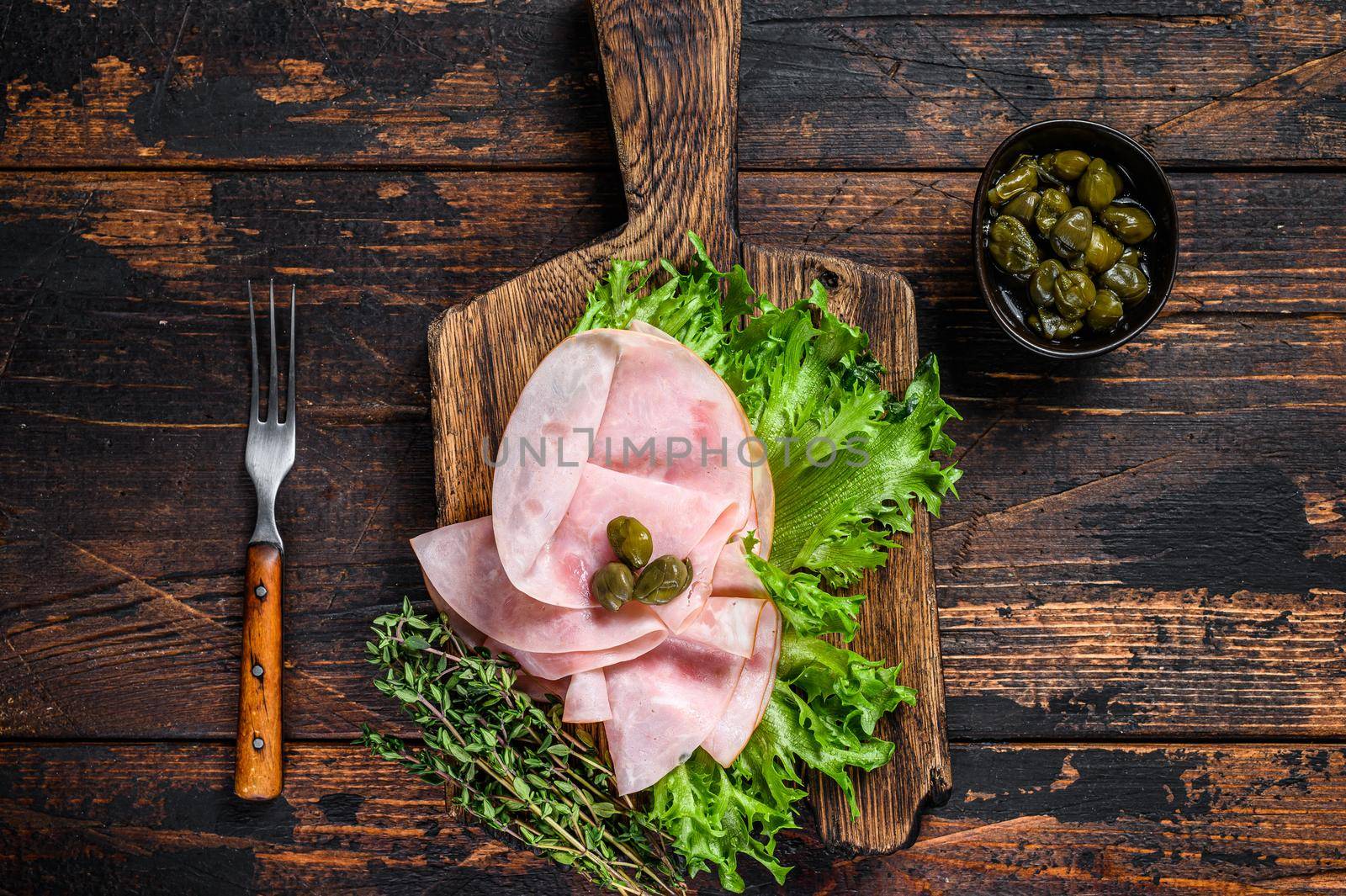 Sliced smoked ham with fresh salad and herbs. Dark wooden background. Top view.